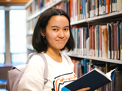 A student in standing in the book stacks in a library