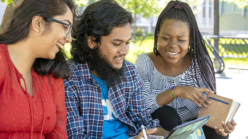 Three diverse students looking at a laptop outside on campus