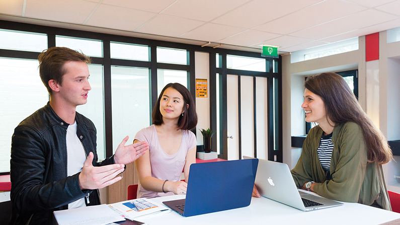 Two students engaged in a friendly chat with an advisor in a room on campus