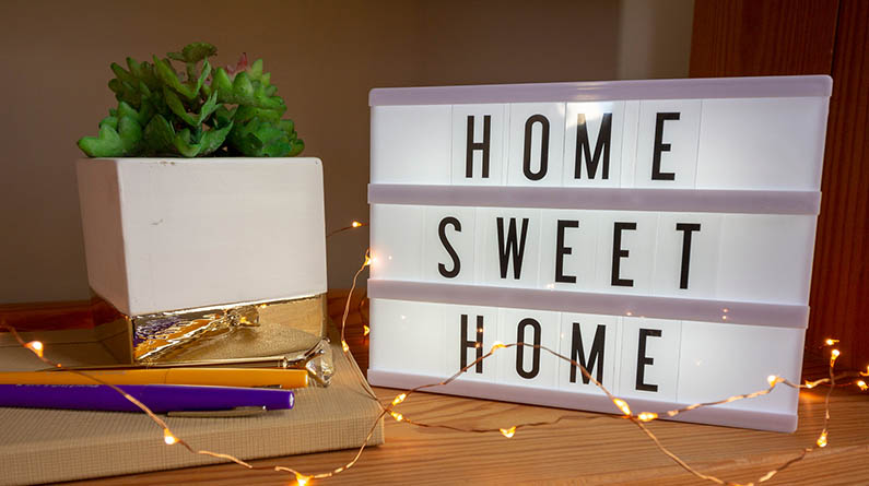 A mini marquee that reads Home Sweet Home that's on top of a desk in a dorm