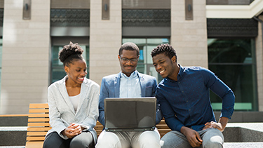 Students seating outside in the university campus and looking at laptop