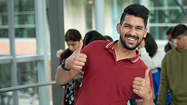 A student in a red polo shirt is smiling and giving thumbs up with both hands.