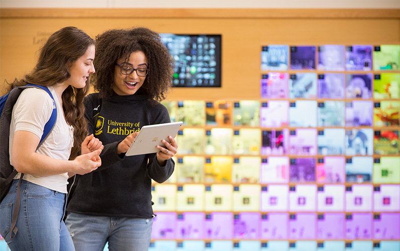 Two students standing and looking at the tablet.